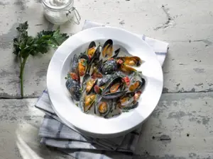 cider braised mussels in white bowl on grey table