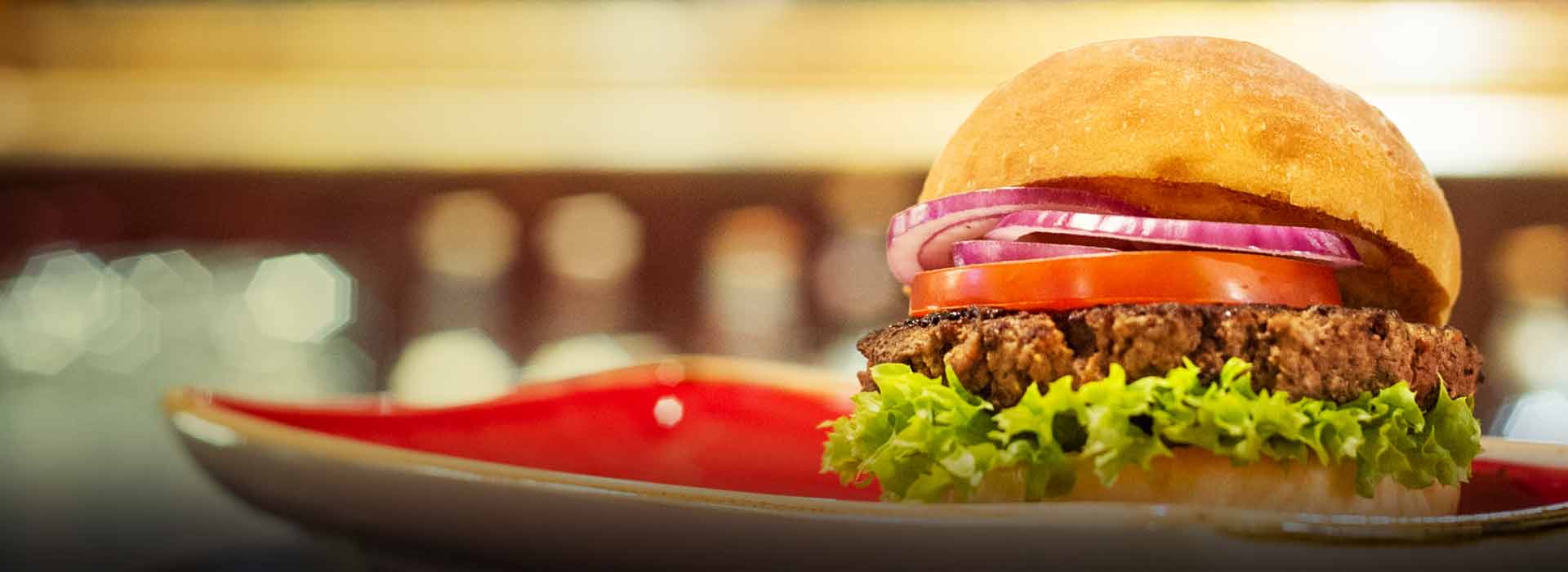 Dressed burger in a bun on a red plate.