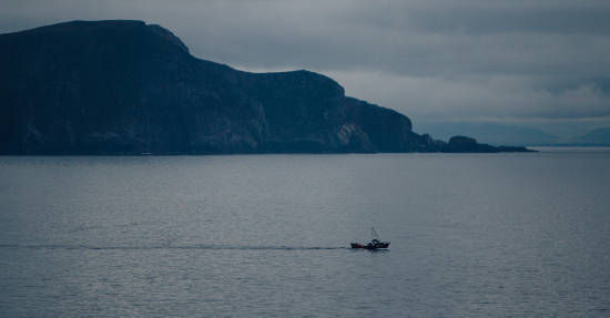 Small fishing boat at sea with sea cliffs and headland in background
